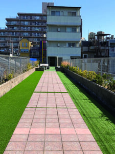 施設の庭園・外構。ピンク色の歩道と緑の芝生が整備された屋外スペース